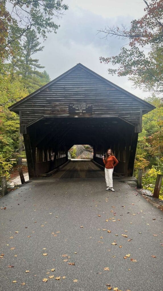 A woman walks through a weathered covered bridge on a foggy New England morning