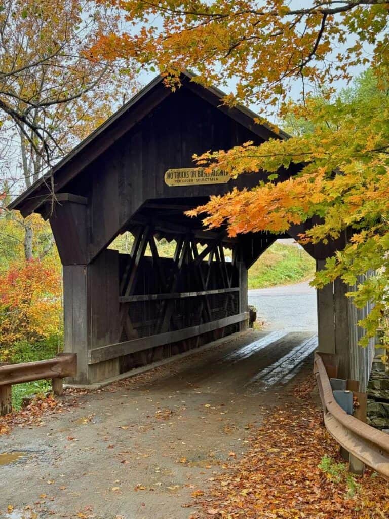 Bright orange leaves frame the entrance to a wooden covered bridge in Vermont

