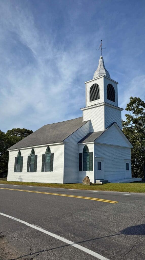 A white steepled church stands along a quiet coastal road in Kennebunkport
