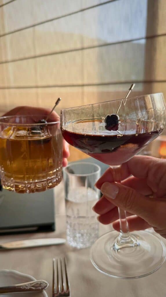 An old fashioned and a Manhattan clinked together over a candlelit table at the Penrose Room