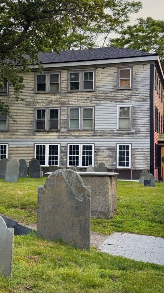 The weathered gray House of the Seven Gables sits beside a Salem cemetery
