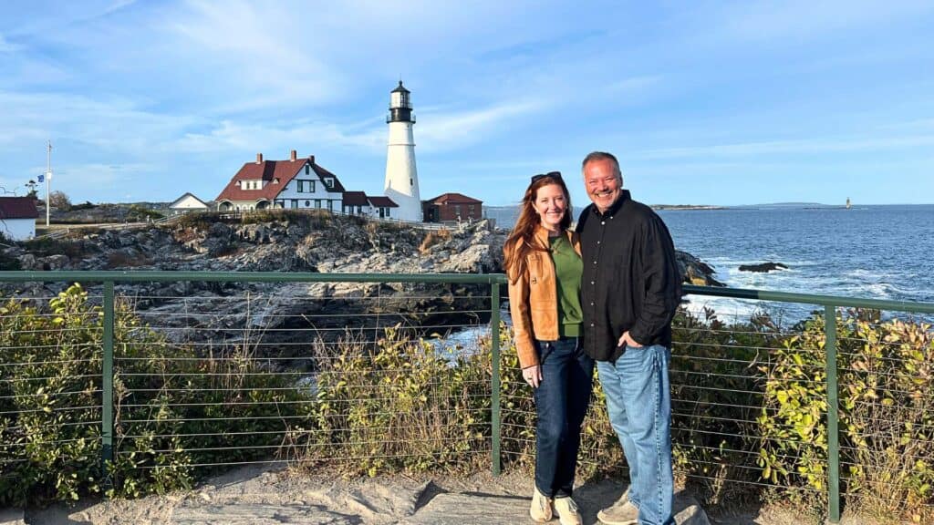 Couple standing at the base of Portland Head Light at golden hour
