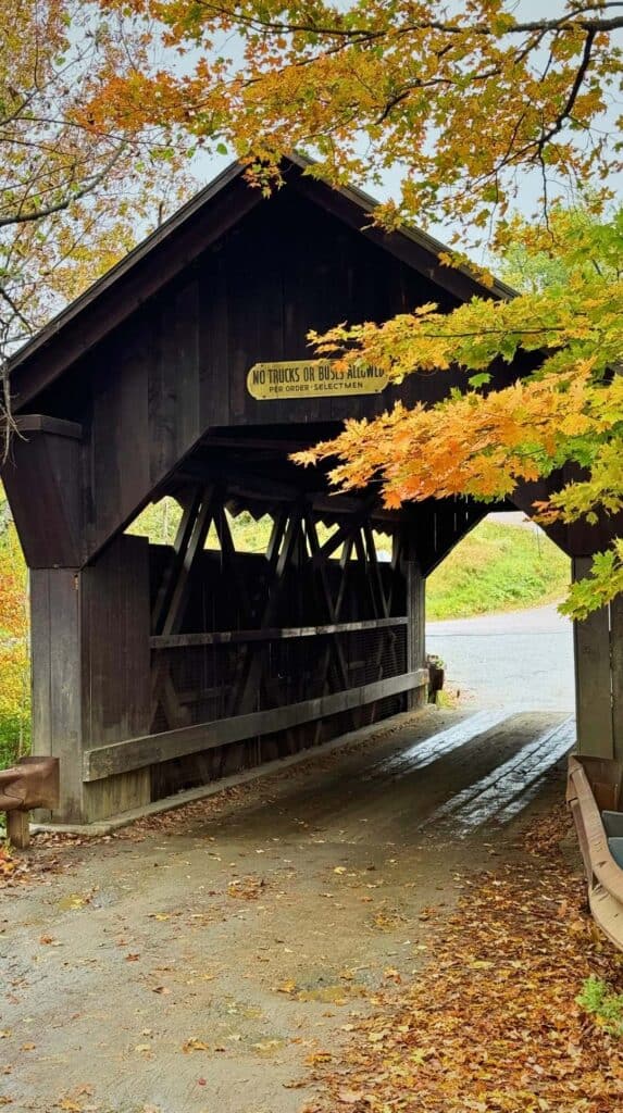 Leaves scatter across the road at the entrance to a Vermont covered bridge
