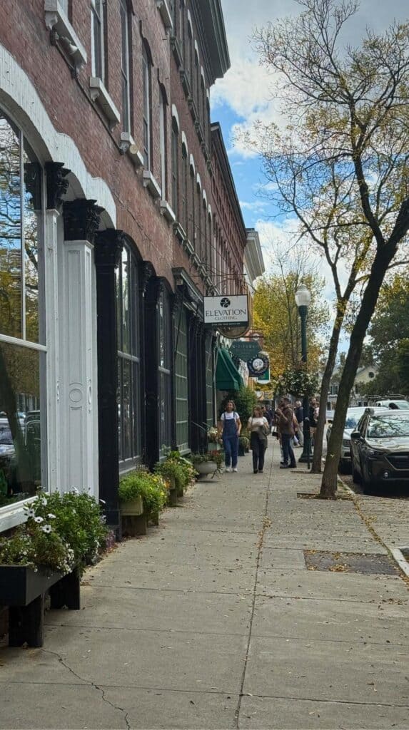 Shoppers stroll a brick sidewalk past storefronts in a historic New England town
