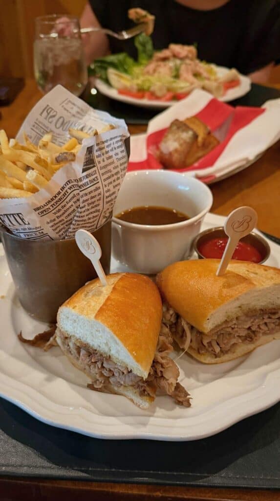 Prime rib French dip on a hoagie with au jus and newspaper-wrapped fries at La Taverne