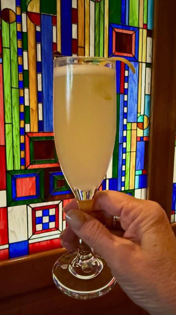 A champagne cocktail held in front of a colorful stained-glass window at La Taverne