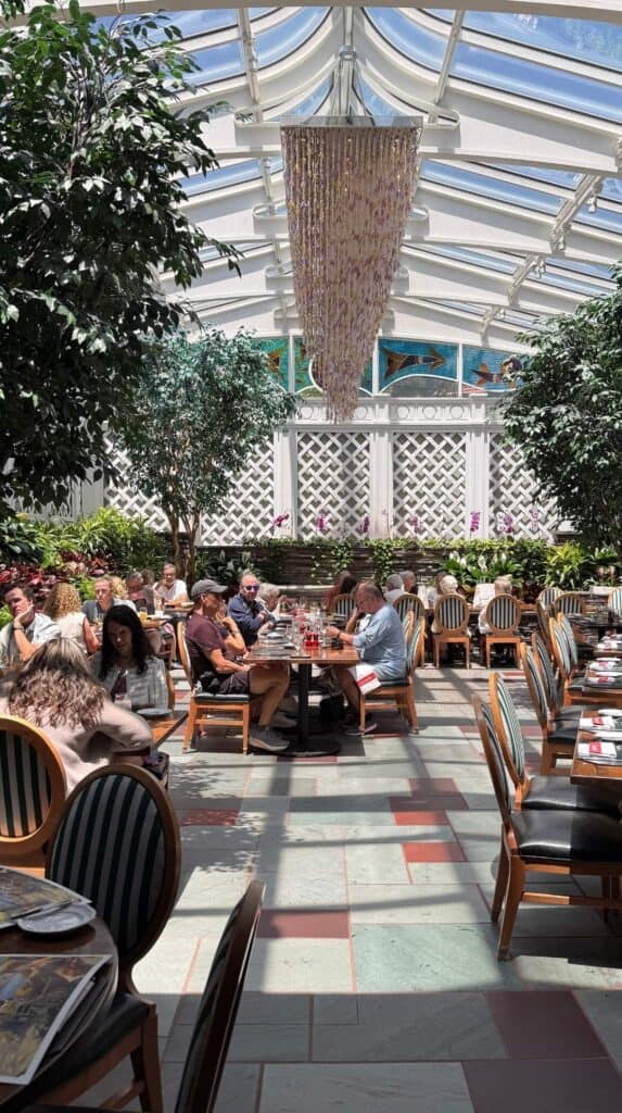 Le Jardin, the glass-roofed garden conservatory with white lattice and live trees at La Taverne