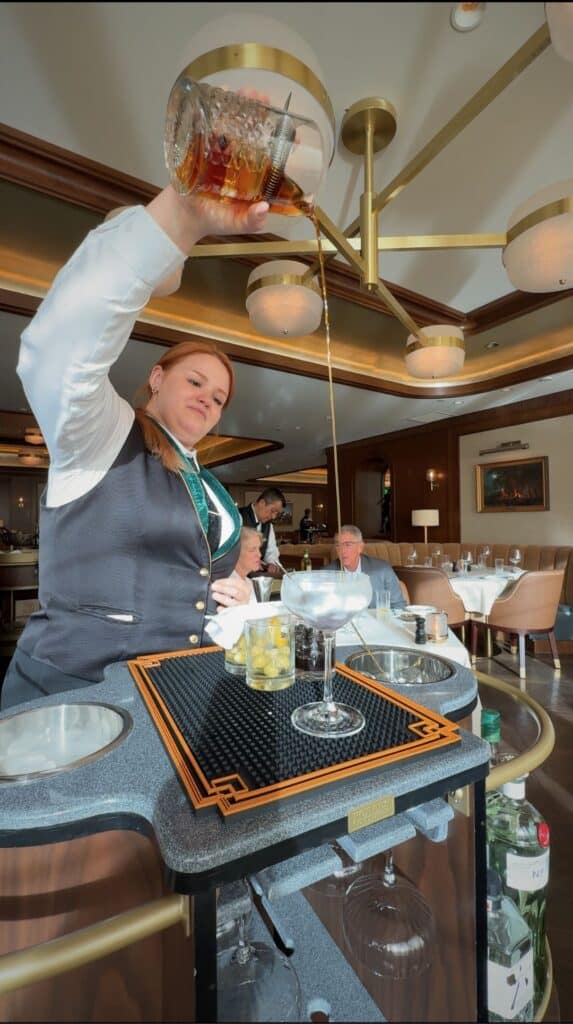 A bartender building a tableside Manhattan on a rolling bar cart at the Penrose Room