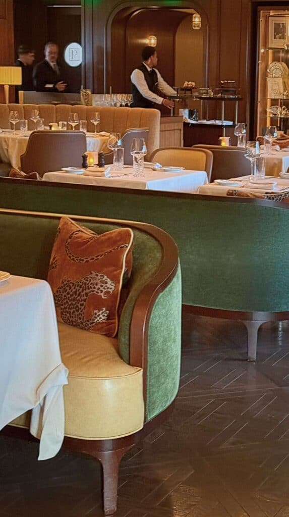 Curved green velvet banquettes, brass accents, and a leopard pillow in the Penrose Room dining room