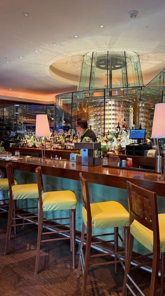 The circular glass wine tower and yellow bar stools at the Broadmoor Summit restaurant bar